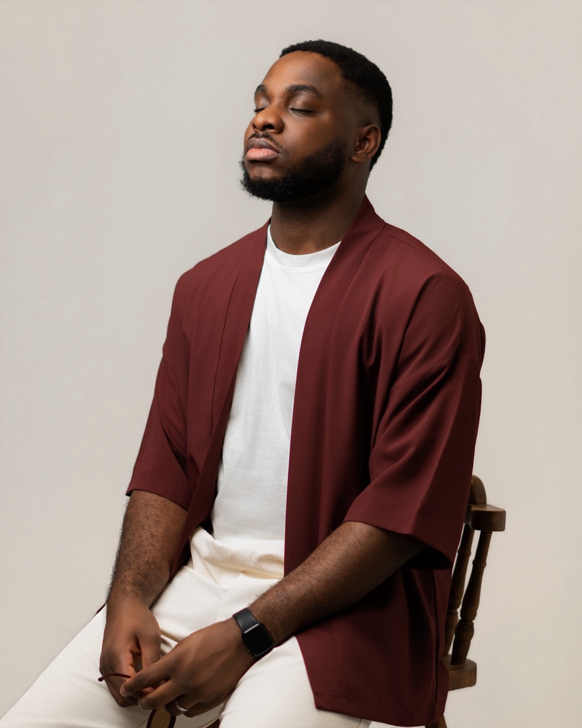 Paul-Emmanuel Ossom seated in a burgundy jacket, eyes closed, head tilted back
